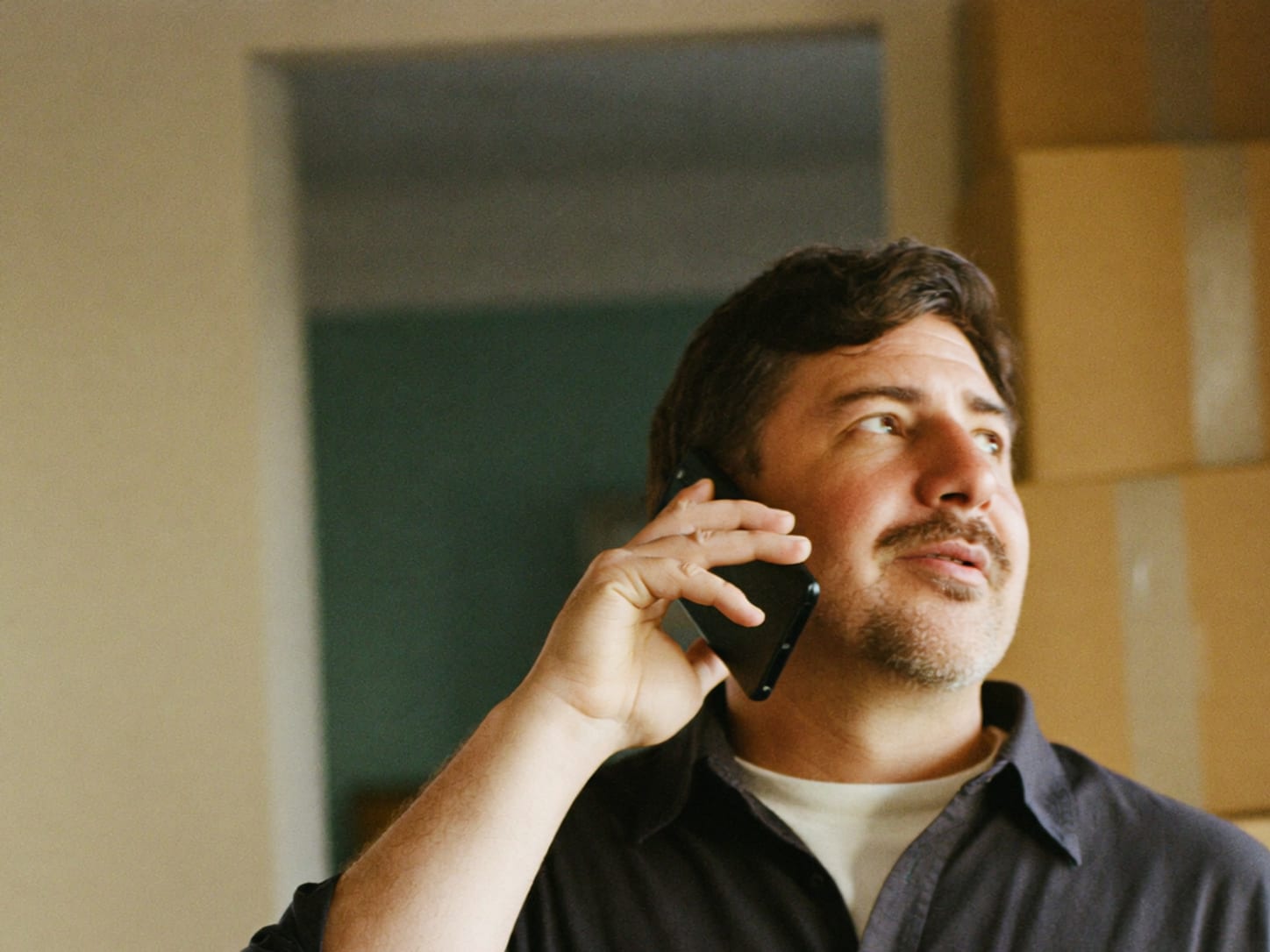 A man talking calmly on the phone in a half-packed home, with moving boxes behind him