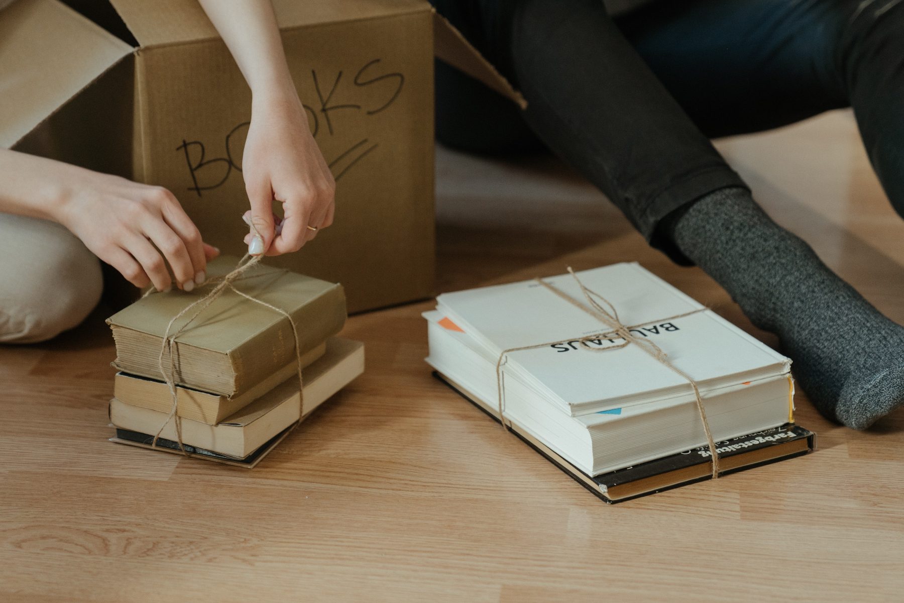 Hands tying a bundle of well-loved books beside a moving box
